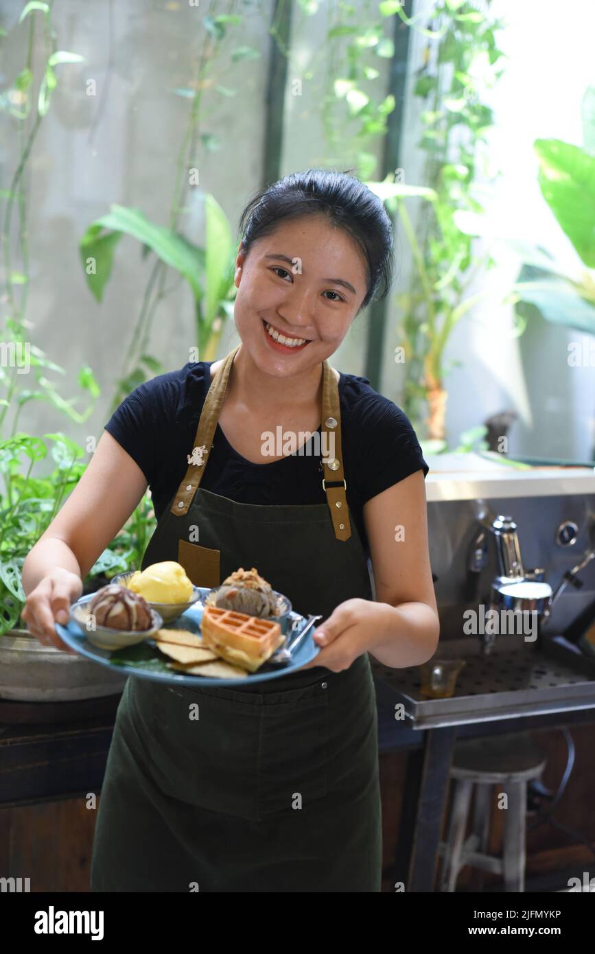 Vietnamesisches Mädchen, das in einem Café hausgemachtes Eis mit Waffeln serviert. Stockfoto