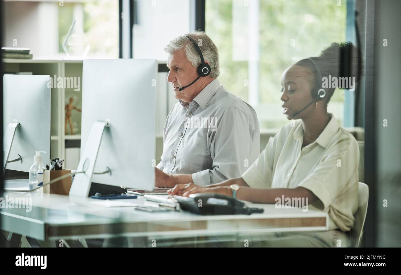 Hart an der Arbeit hier drüben. Aufnahme von zwei Call Center-Agenten, die zusammen im Büro sitzen und ihre Computer nutzen. Stockfoto