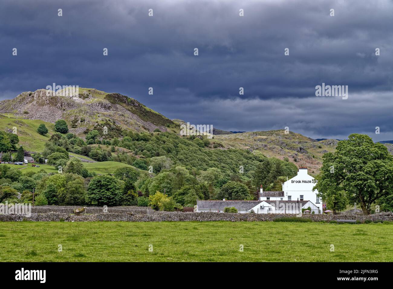 Das Brook House Inn, eingebettet zwischen dramatischen Fjells mit dunklen Sturmwolken, Eskdale Lake District Cumbria England, Großbritannien Stockfoto