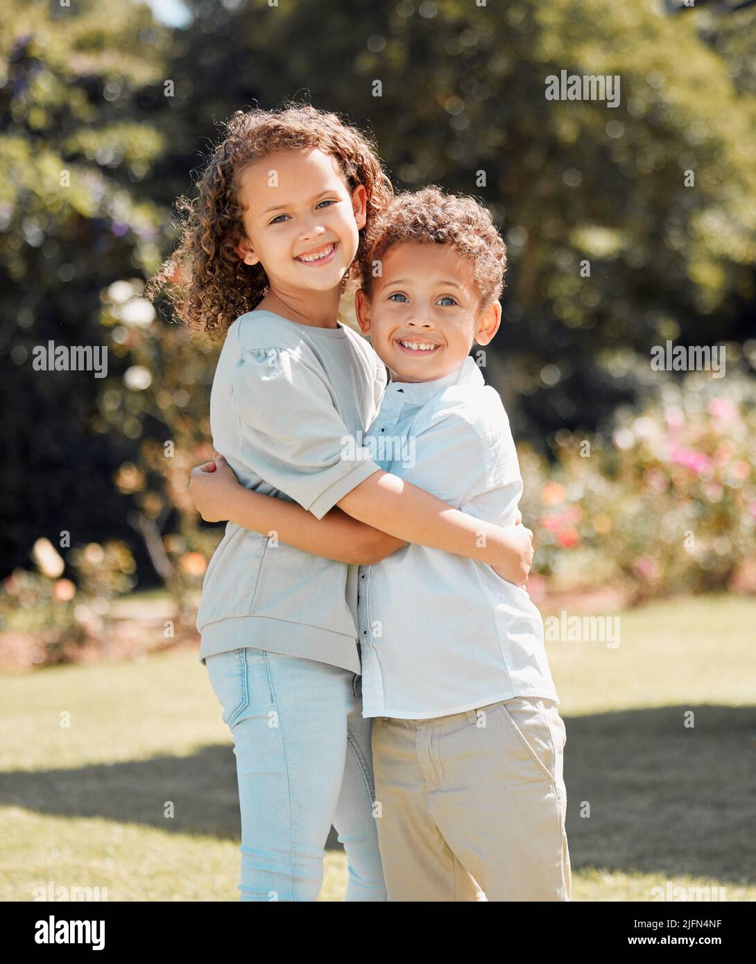 Porträt eines Bruders und einer Schwester gemischter Rassen, die lächeln, sich in einem Garten draußen umarmen und stehen. Hispanische männliche und weibliche Geschwister zeigen Stockfoto