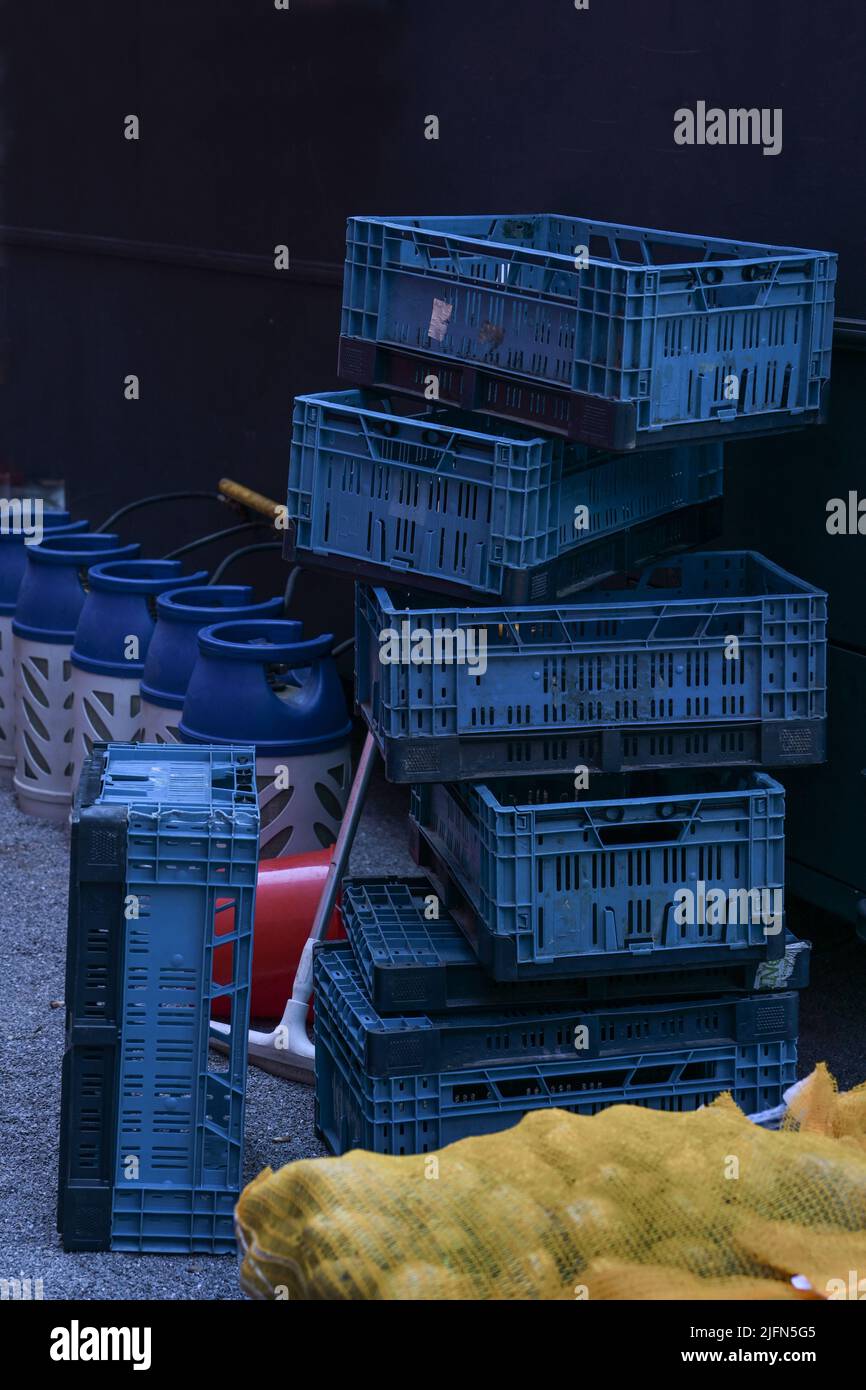 Blaue Kunststoff-Transportboxen, Kartoffelsack und Fässer für Gasflaschen auf der Rückseite eines Chips Shop Food Track, dunkler Hintergrund, Kopierraum, ausgewählter FOC Stockfoto