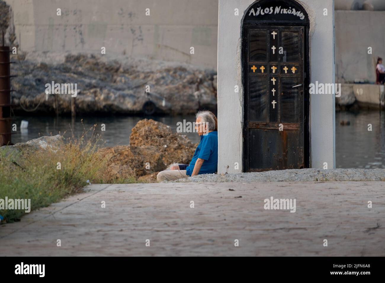 Ein alter Mann sitzt an der Seite einer kleinen Kapelle und starrt den Horizont der Ägäis Stockfoto