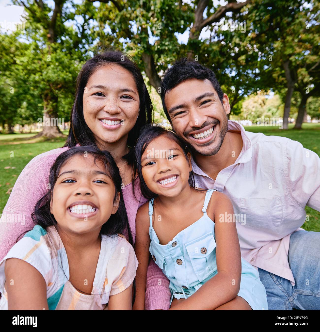Porträt einer glücklichen asiatischen Familie im Park. Familienportrait von Ehemann und Ehefrau, die mit ihren Töchtern sitzen und ihre Freizeit genießen Stockfoto