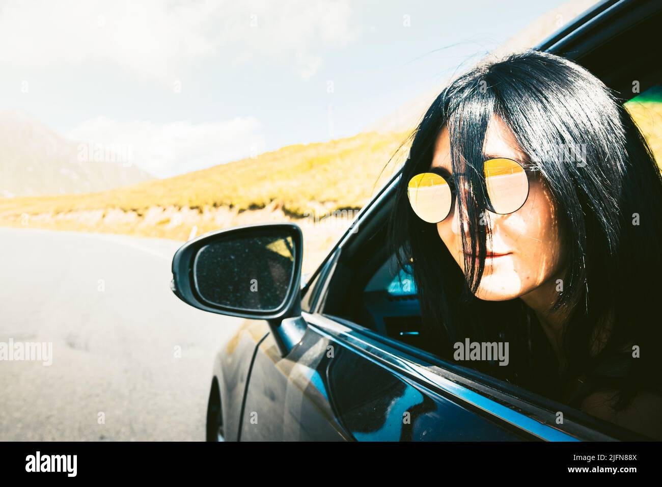 Schwarze kaukasische Frau mit dem Gesicht vom Autofenster schaut während der Fahrt direkt zur Kamera. Sichere Fahrt am Urlaubsziel. Reiseversicherung Mock up conce Stockfoto