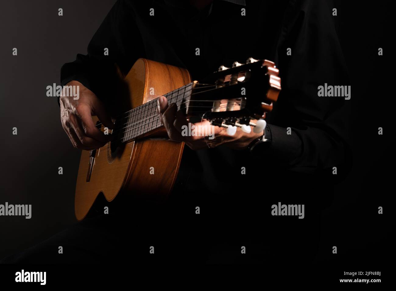 Spanische klassische Gitarre und die Hände des Gitarristen nah auf einem schwarzen Hintergrund mit Kopierraum Stockfoto