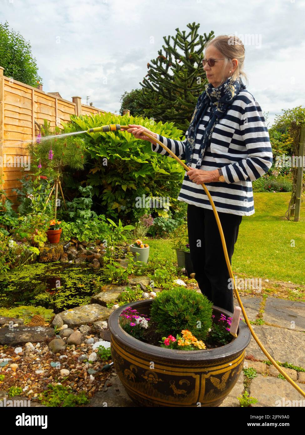 Ältere Dame Frau Gärtner mit einem Schlauch zu einen Garten in North