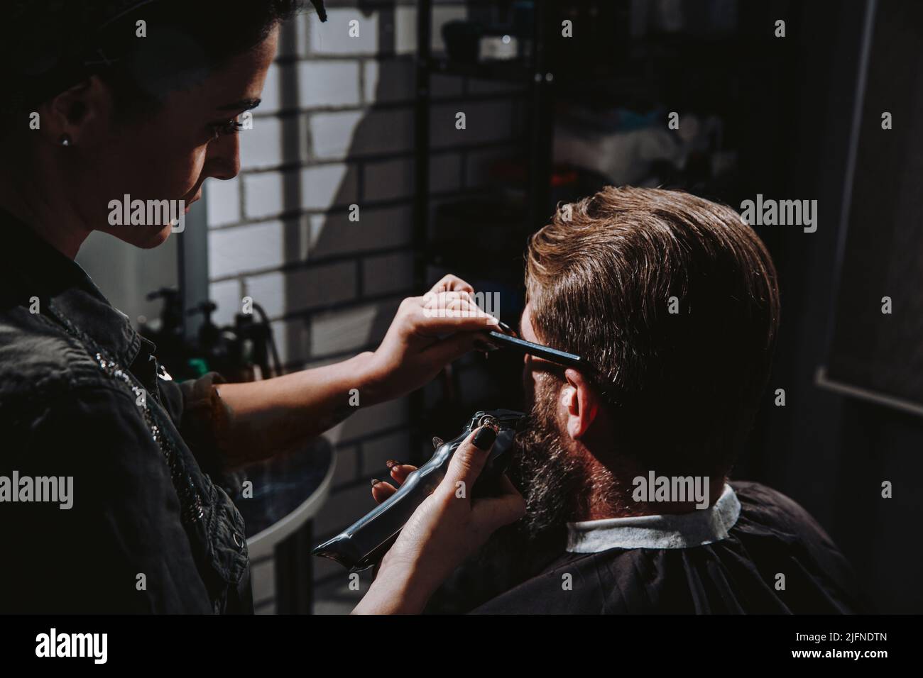 Junge Barbierin, die im Friseursalon einen Bartmann abschneidet. Selbstpflege, maskuline Schönheit. Stockfoto