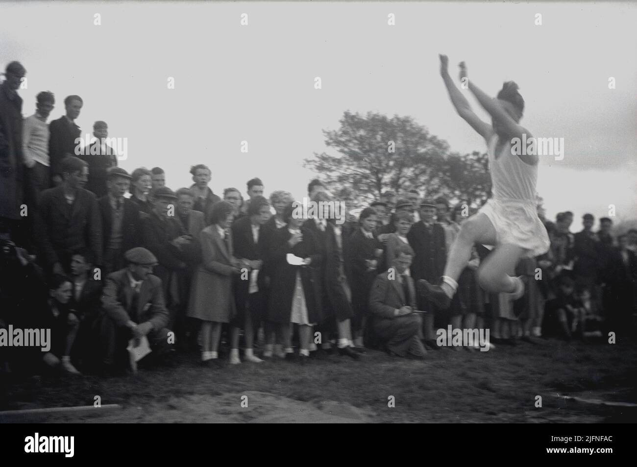 1952, historisch, ein älterer männlicher Student, der den Weitsprung machte, beobachtet von einer Gruppe von Erwachsenen und Schulkindern, Schottland, Großbritannien. Stockfoto