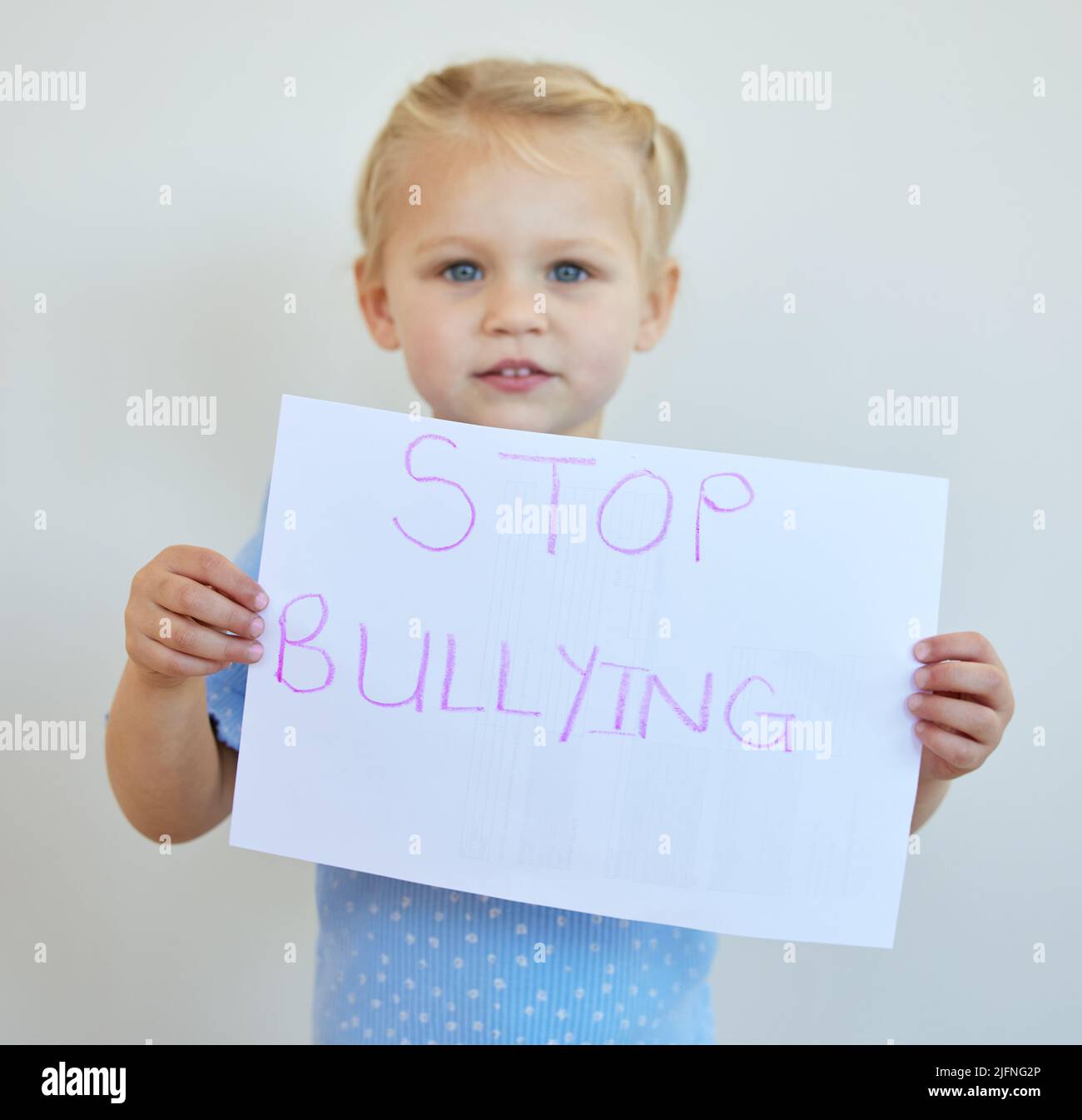 Kleines Mädchen, das mit einem Schild gegen Mobbing protestiert. Entzückendes kaukasisches Kind, das allein steht und ein Protestplakat vor weißem Hintergrund hält Stockfoto