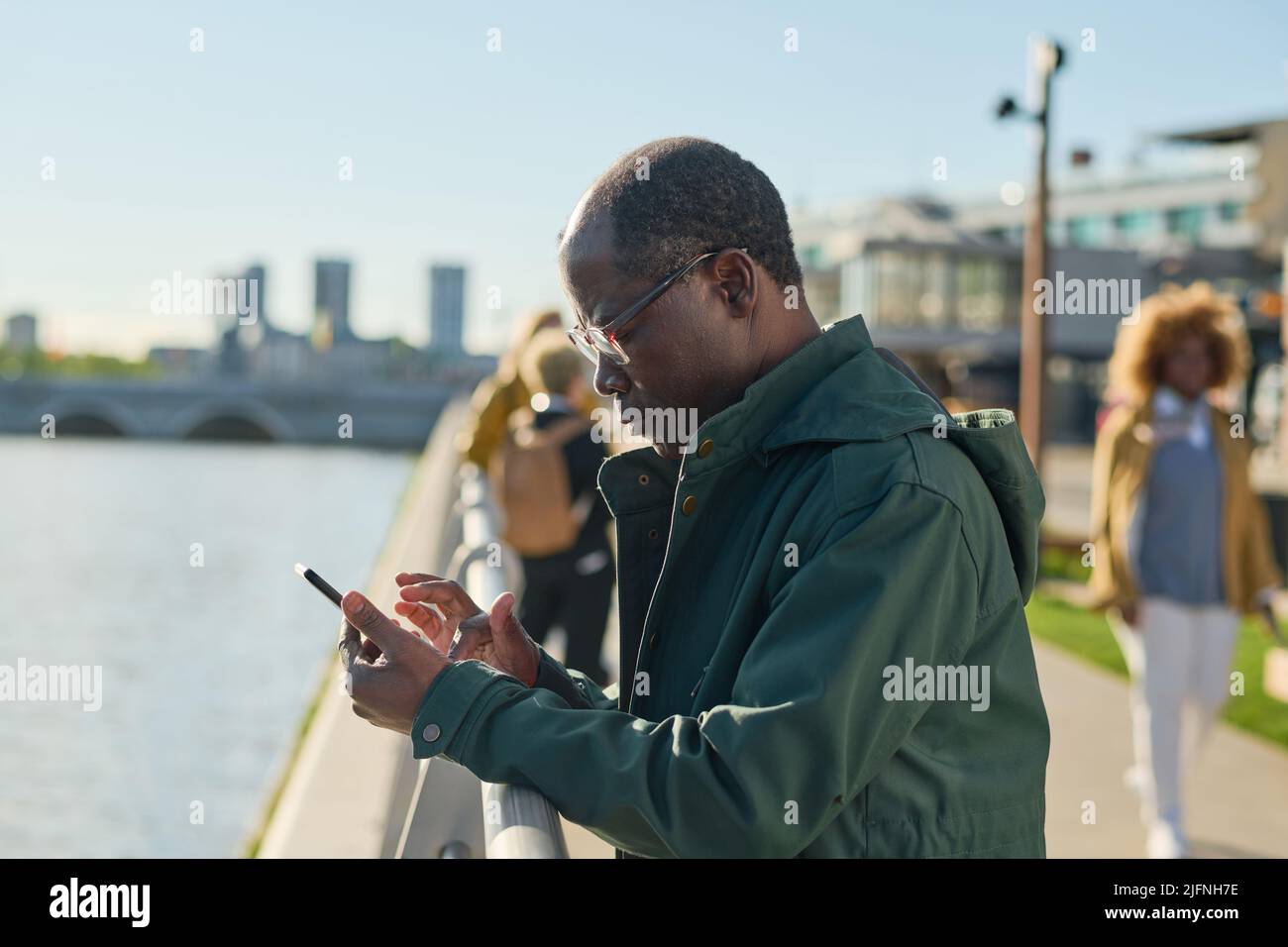 Afrikanischer reifer Mann in einer Brille, der eine Nachricht auf seinem Mobiltelefon tippt, das im Freien in der Stadt steht Stockfoto