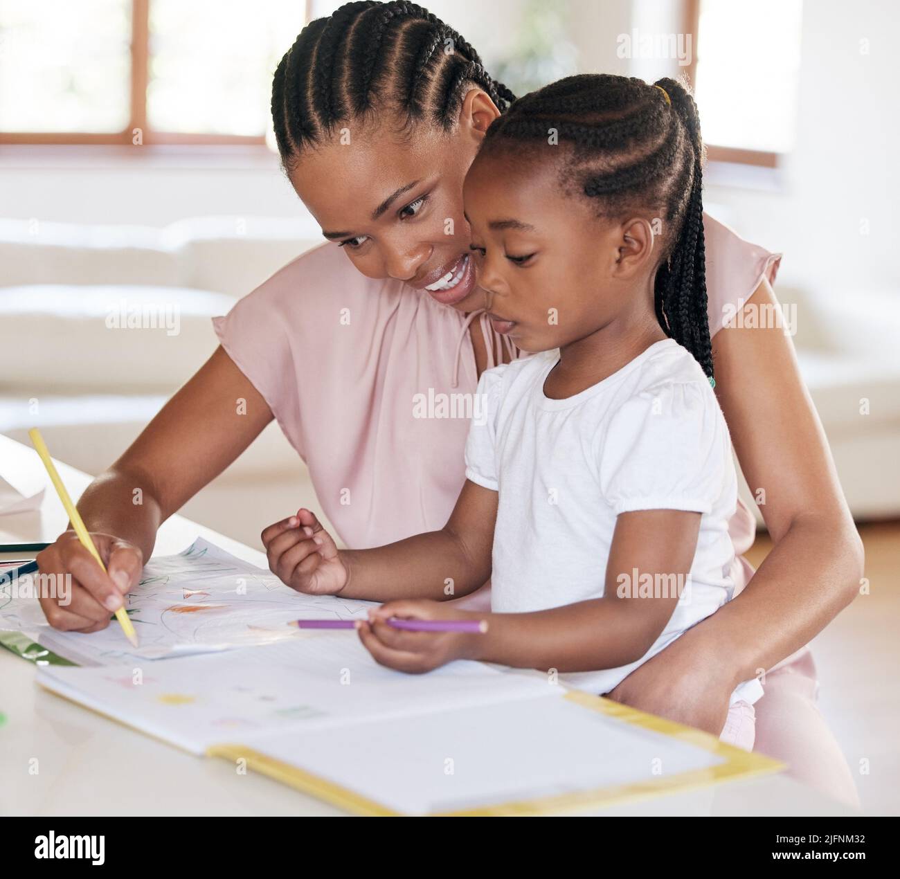 Junge afroamerikanische Mutter hilft ihrer Tochter bei Hausaufgaben zu Hause. Kleines Mädchen zeichnen mit ihrer Mutter zu Hause. Schwarze Frau zeigt ihre Tochter Stockfoto