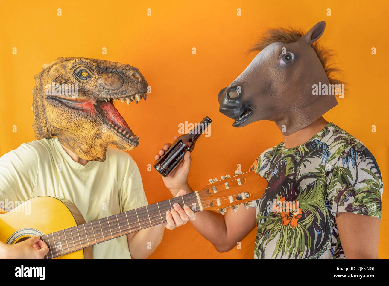 Glückliche Freunde, die Spaß haben Gitarre zu spielen und Bier zu trinken, tragen Tierkopfmasken auf orangefarbenem Hintergrund isoliert.Party paar Freunde, surreal concep Stockfoto