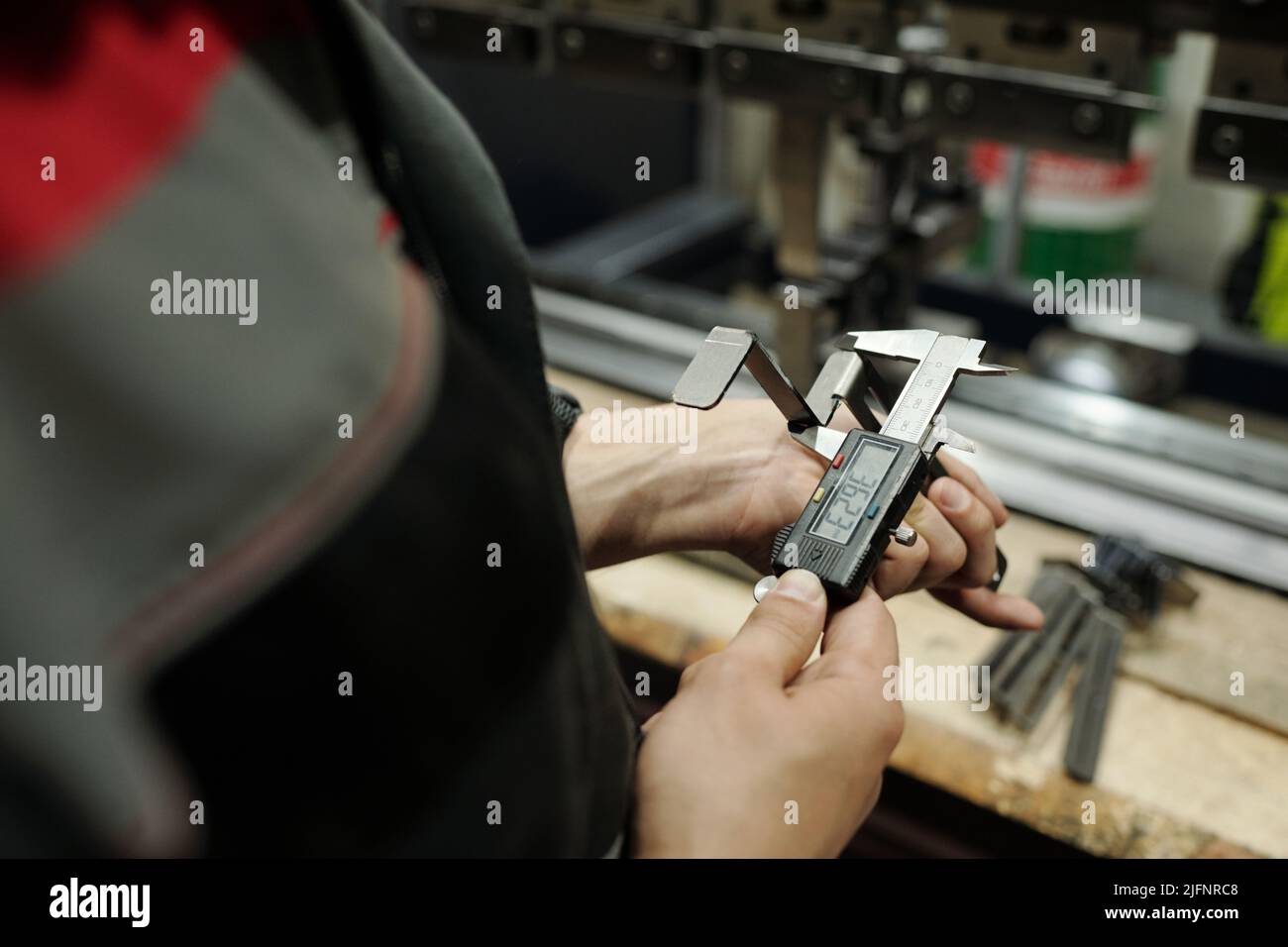 Hände eines männlichen Ingenieurs, der Details aus Edelstahl mit Bremssätteln mit elektronischem tableau nach Arbeitsplatz misst Stockfoto