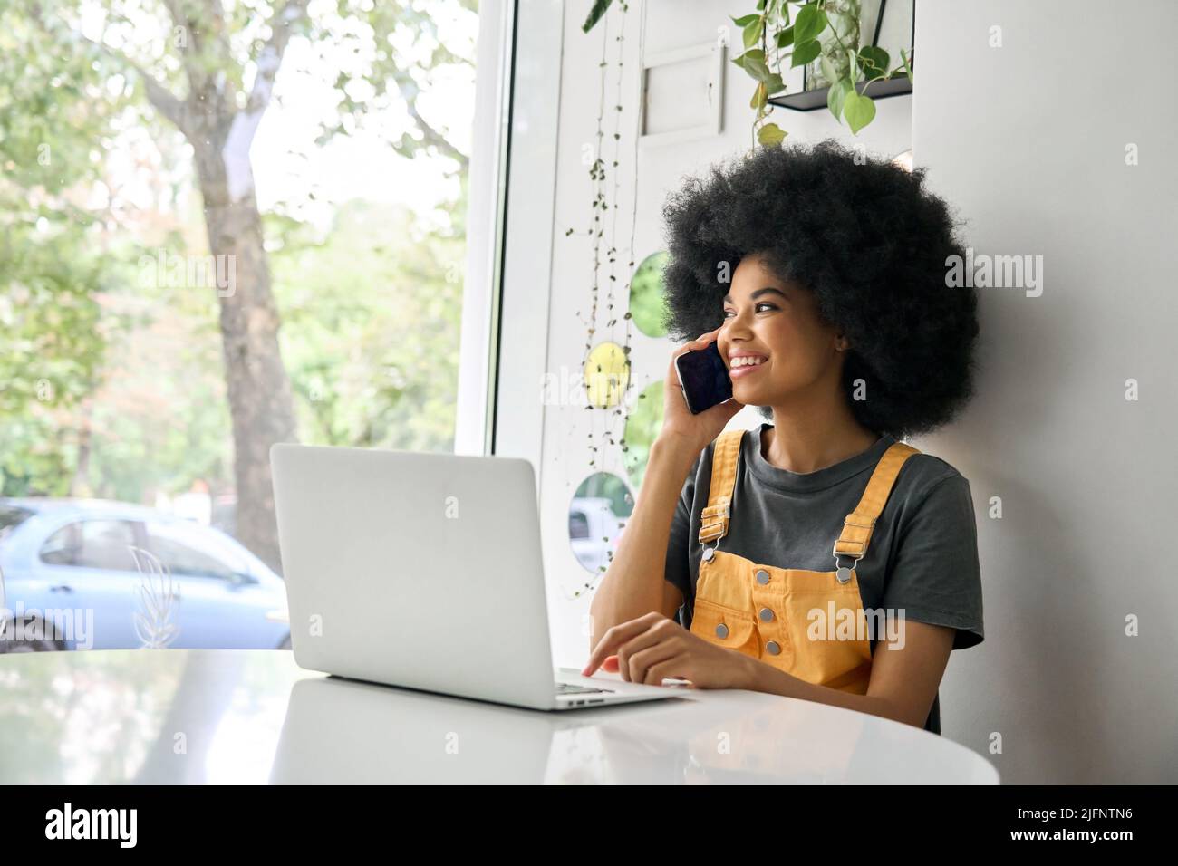 Junge glückliche Frau, die im Café mit einem Laptop telefoniert. Stockfoto