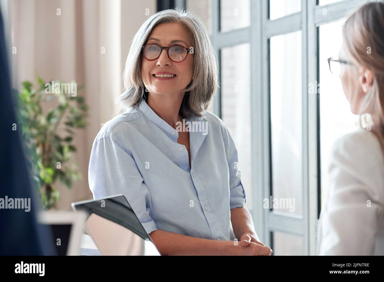 Lächelnde ältere Trainerin, die mit Studenten oder Praktikanten kommuniziert Stockfoto