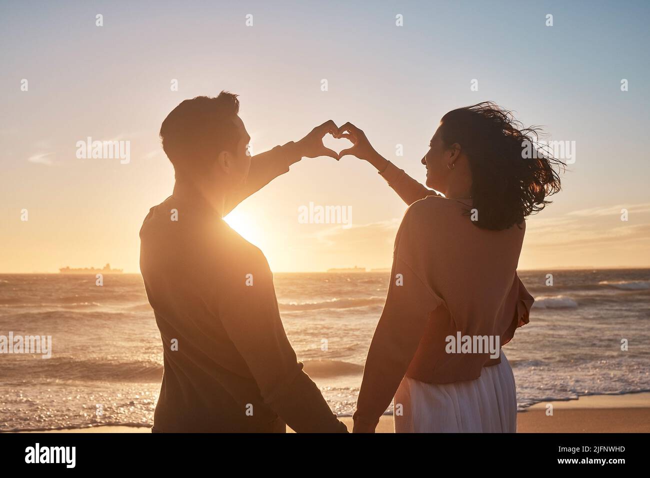 Biracial Paar hält ihre Hände in einer Herzform am Strand zusammen. Biracial Paar hält ihre Hände in einer Herzform am Strand zusammen Stockfoto