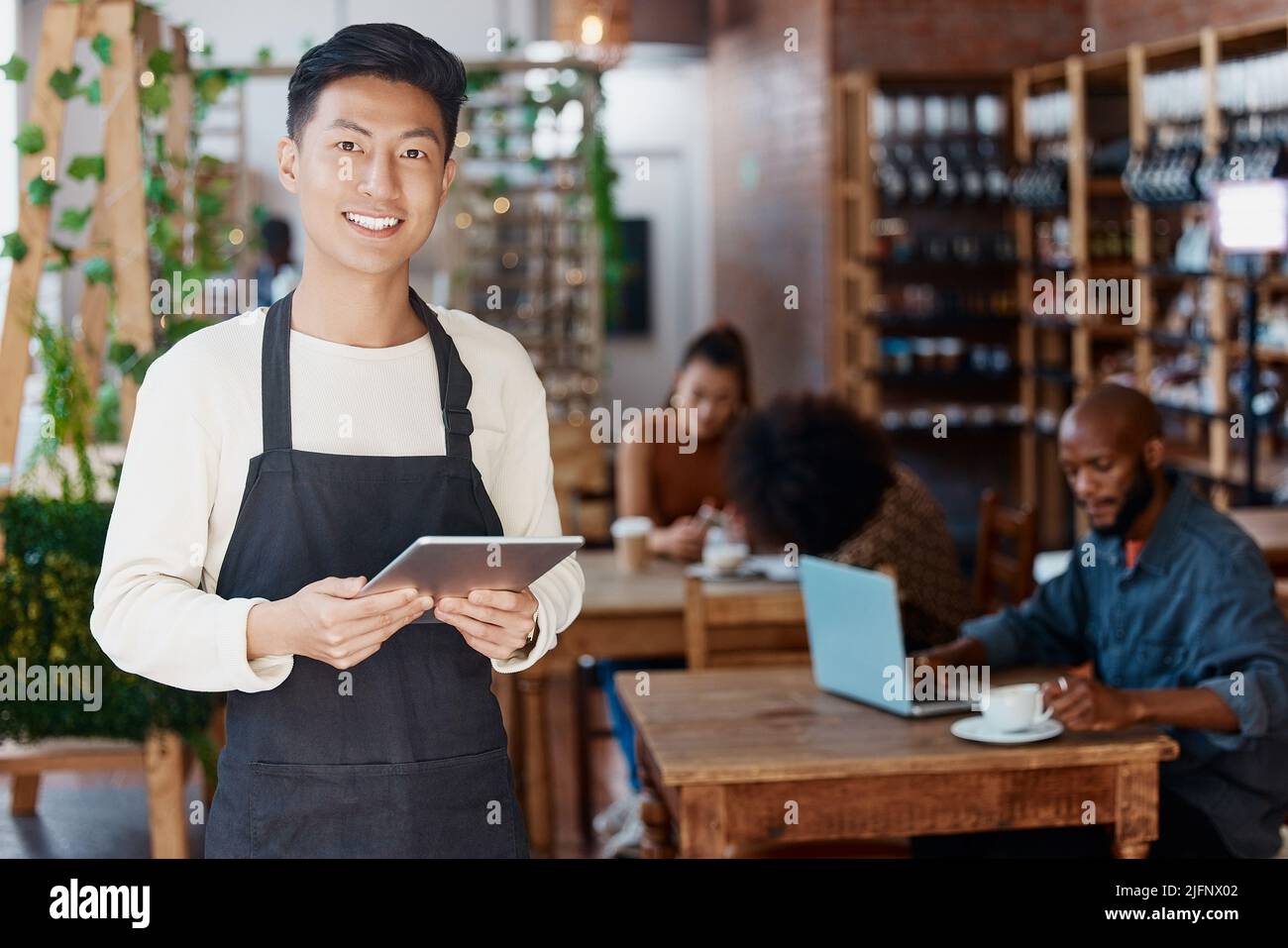 Porträt eines lächelnden asiatischen Kleinunternehmers in seinem Restaurant, der ein drahtloses digitales Tablet in der Hand hält. Junger Geschäftsmann mit einem digitalen Tablet zu tun Stockfoto