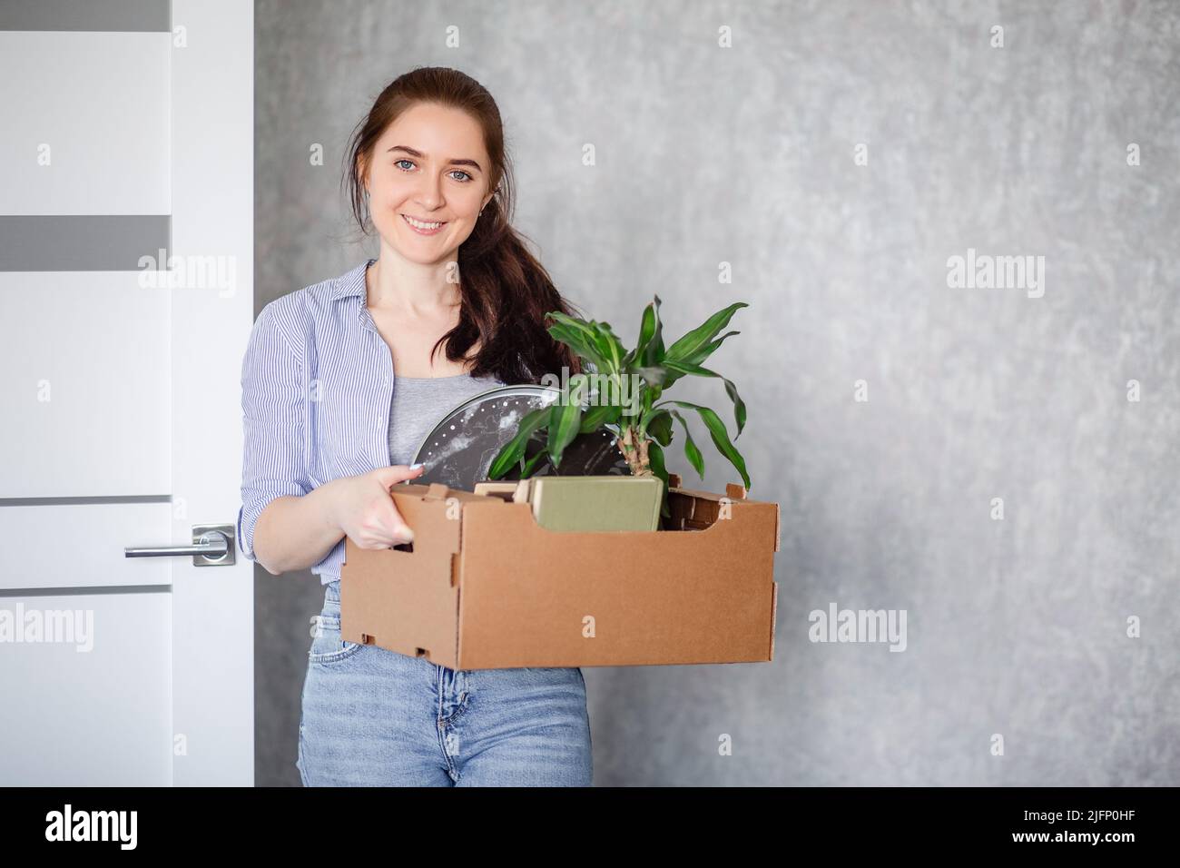 Eine junge Brünette ist glücklich mit der Hausarmierung. Ein Mädchen hält einen Karton mit Dingen, die in eine neue Wohnung an einem neuen Arbeitsplatz umziehen. Stockfoto