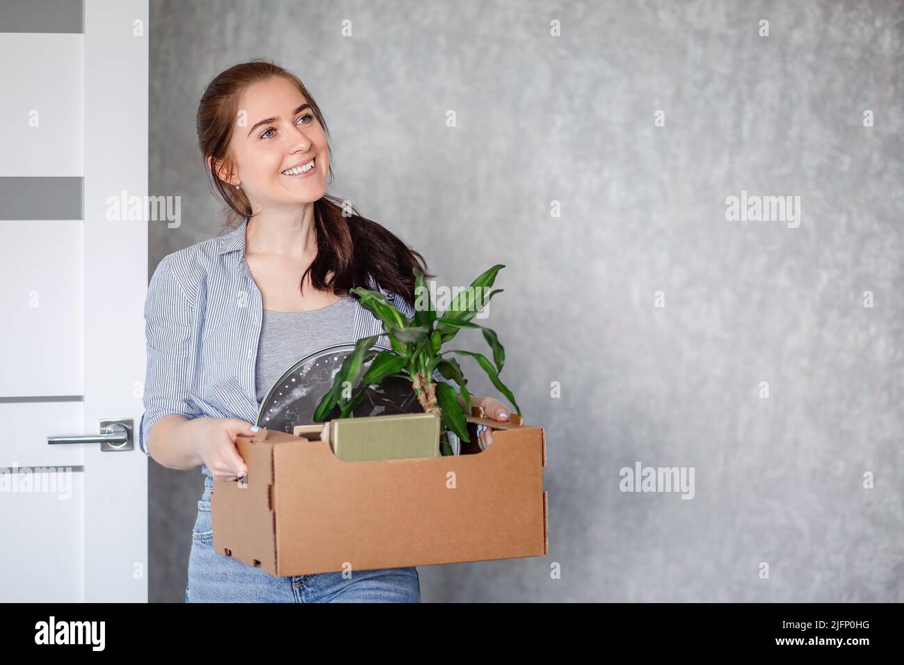 Eine junge Brünette ist glücklich mit der Hausarmierung. Ein Mädchen hält einen Karton mit Dingen, die in eine neue Wohnung an einem neuen Arbeitsplatz umziehen. Stockfoto