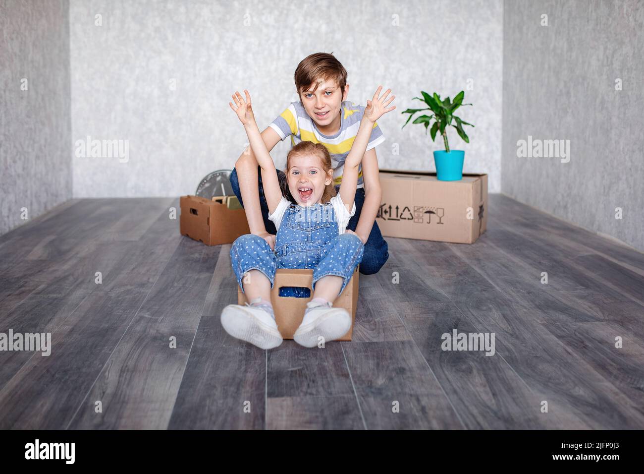 Bruder reitet Schwester in einem Karton. Kinder spielen mit Kisten zu Hause in Quarantäne. Ein Junge und ein Mädchen sind in eine neue Wohnung gezogen und sind es Stockfoto