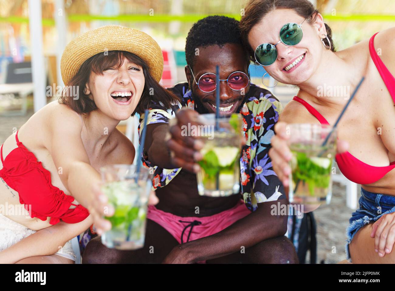Eine multiethnische Gruppe von drei Personen, ein afrikanischer Mann und zwei kaukasische Frauen, die Spaß beim Cocktailtrinken haben und das Toasten mit frisch vereisten coc feiern Stockfoto