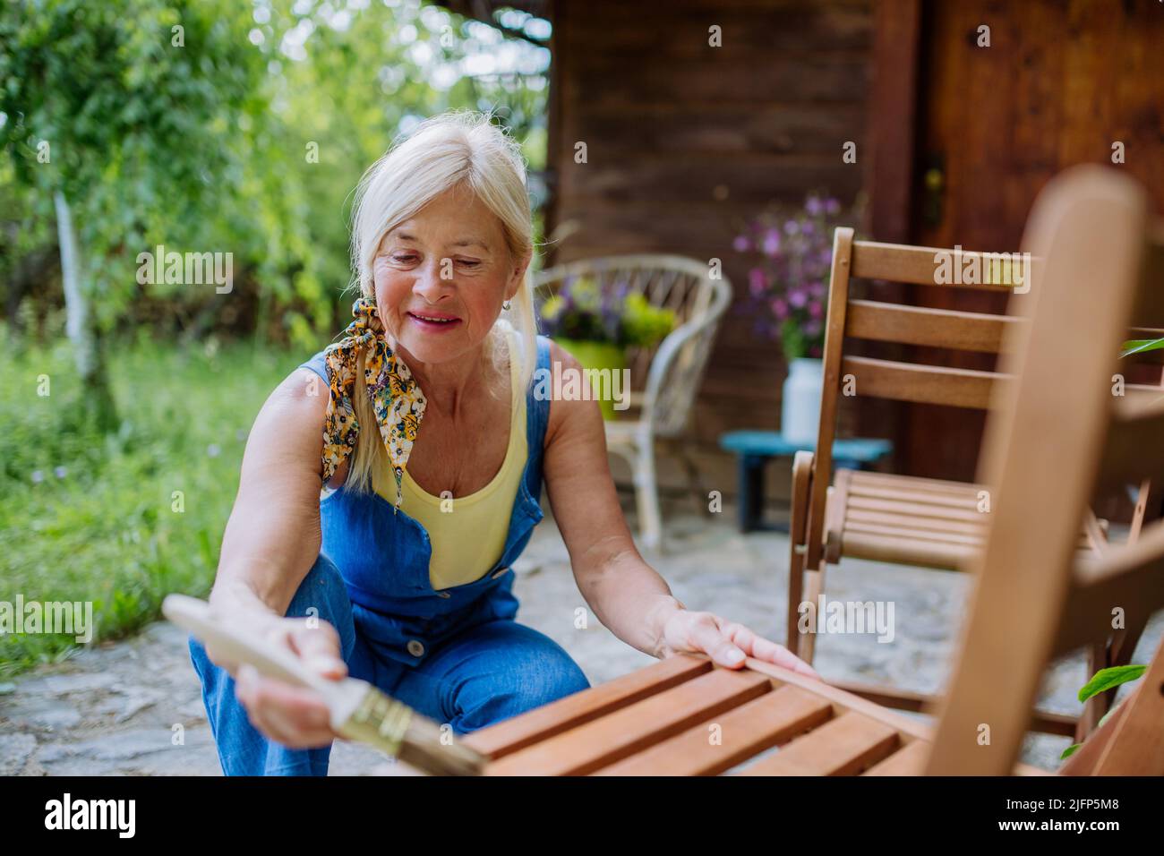 Ältere Frau putzt und renoviert Gartenmöbel und bereitet den Garten für den Sommer vor Stockfoto