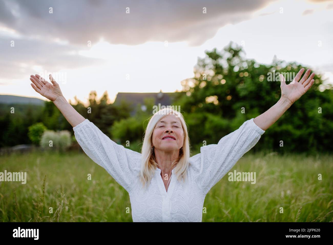 Ältere Frau mit ausgestreckten Armen und Gesicht nach oben im Park am Sommertag, psychische Gesundheit Konzept. Stockfoto
