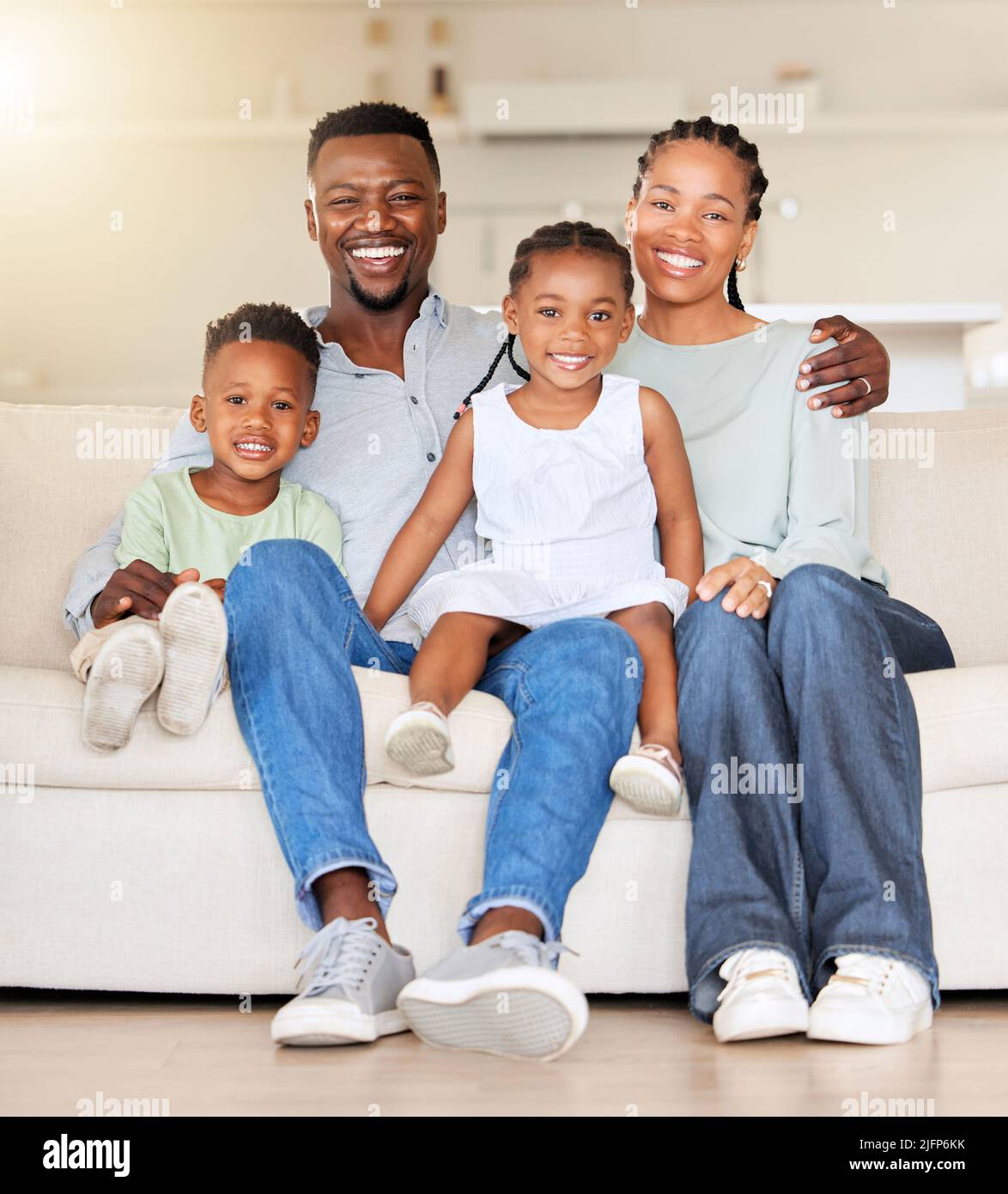 Porträt einer glücklichen afroamerikanischen Familie mit zwei Kindern, die zu Hause auf der Couch sitzen. Liebenswert kleines Mädchen und Junge sitzen mit ihrer Mutter und Stockfoto