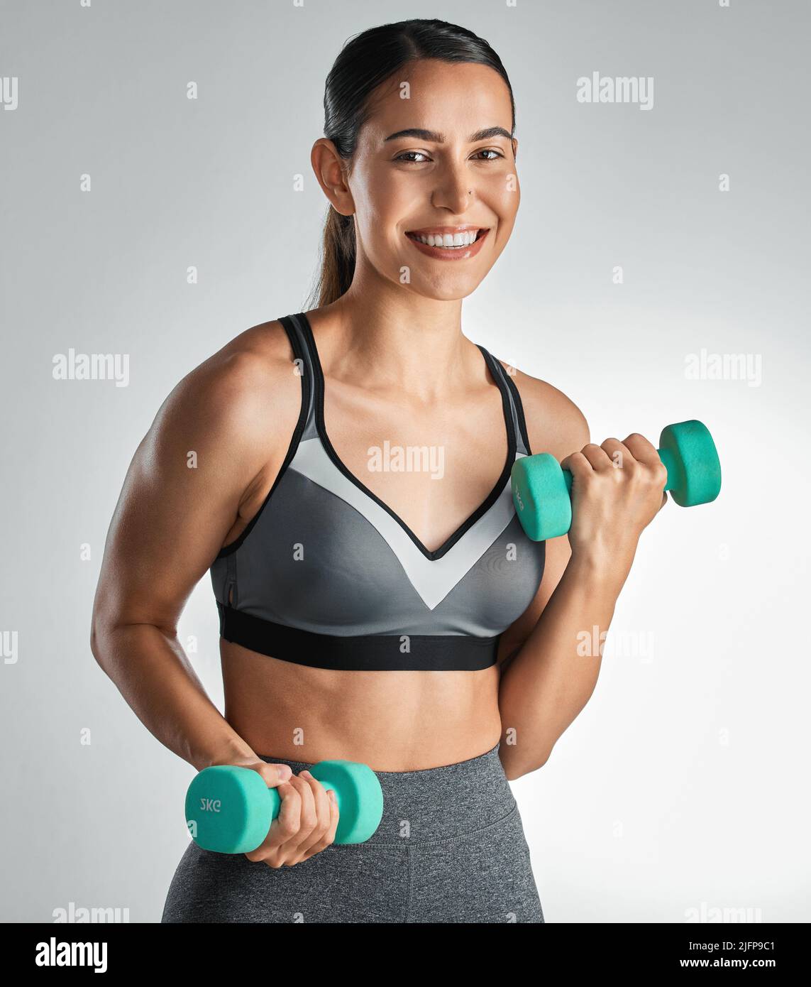 Bereit für eine Ganzkörperstimmung. Studioportrait einer sportlichen jungen Frau, die mit Kurzhanteln vor grauem Hintergrund trainiert. Stockfoto