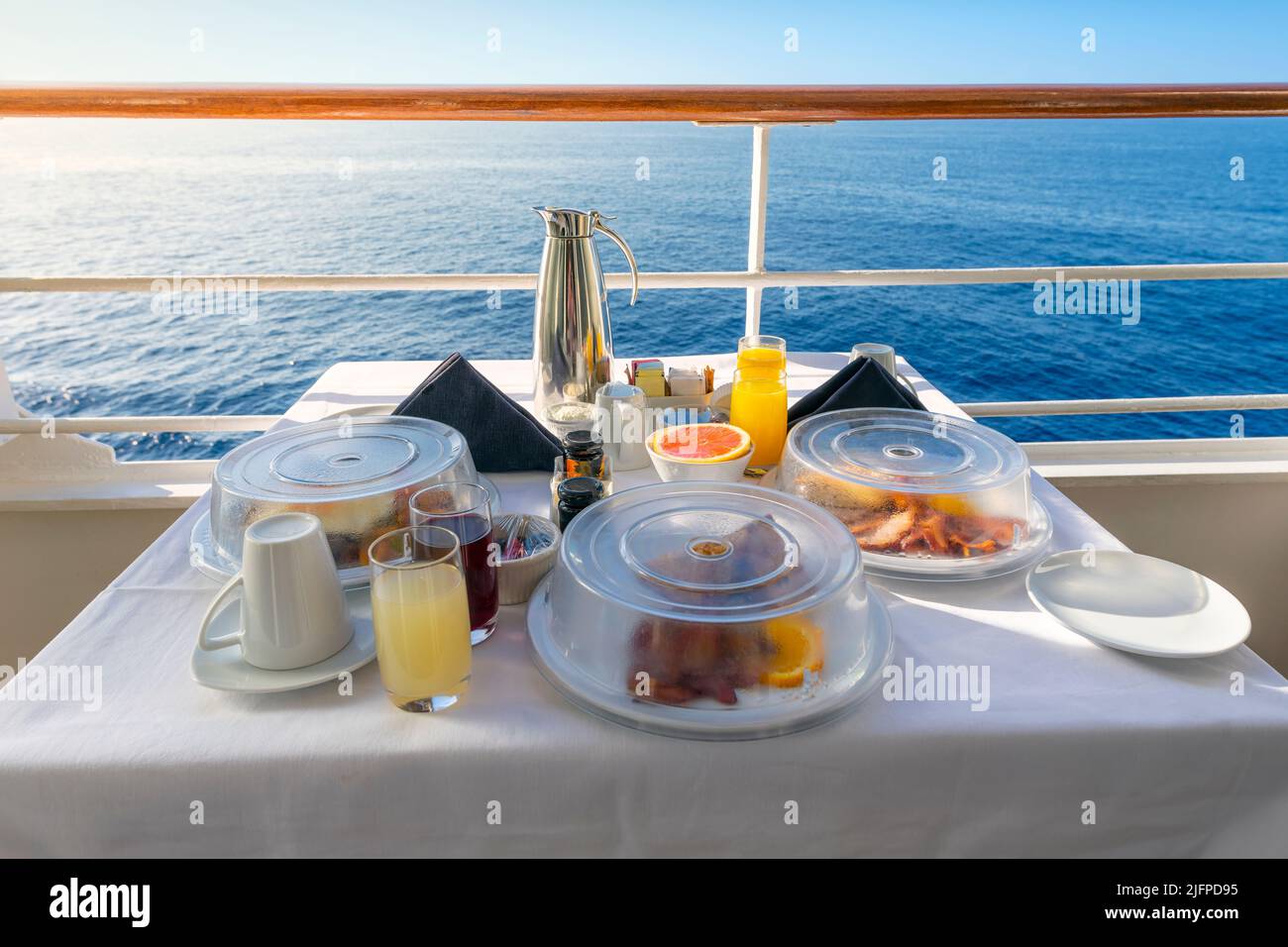Ein komplettes Frühstück mit Zimmerservice auf dem Balkon einer Kreuzfahrt-Kabine auf dem Meer inklusive Saft, Kaffee und komplette Mahlzeiten auf einem sonnigen Luxusurlaub auf dem Meer. Stockfoto