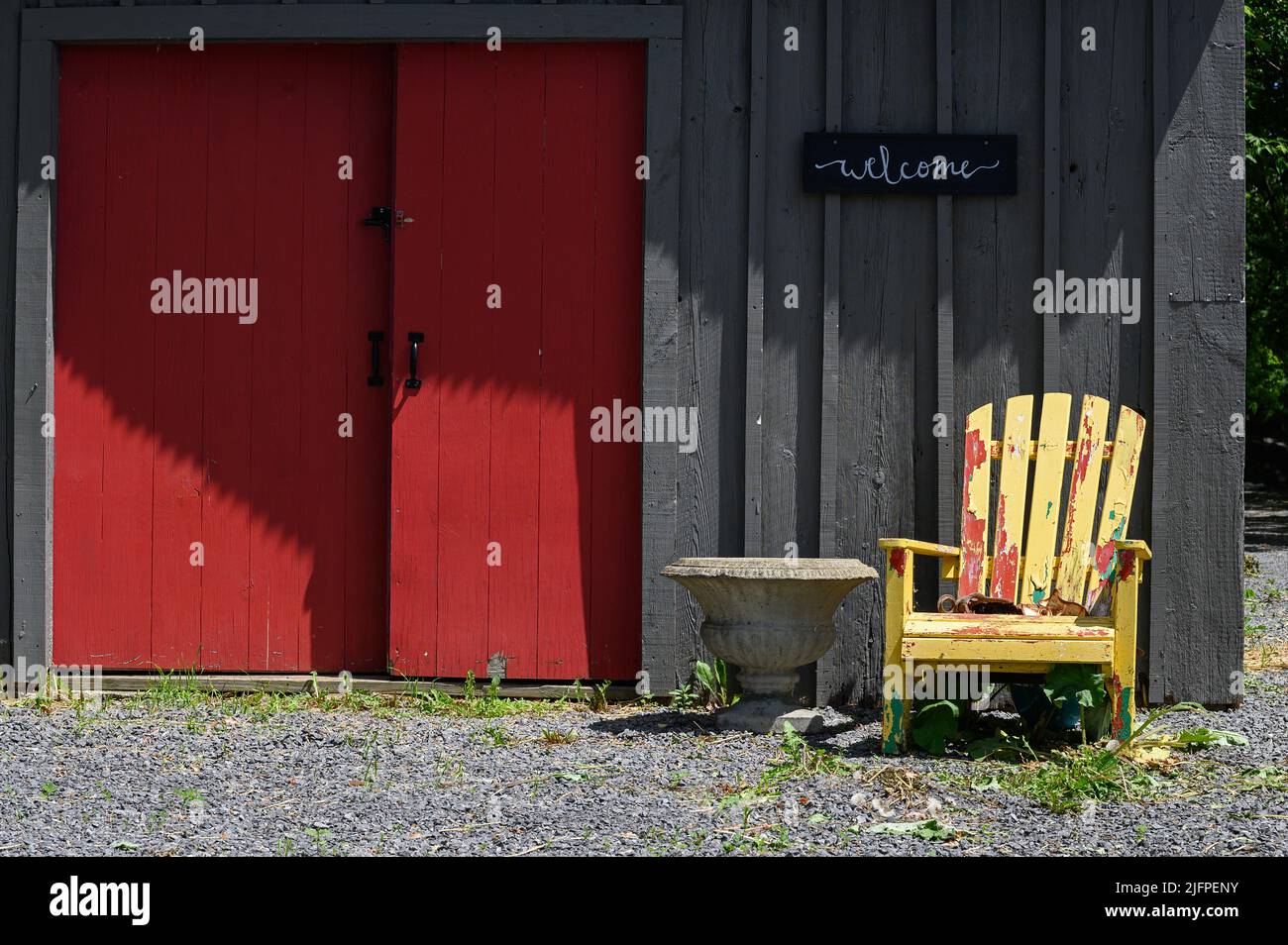 Friedliche Szene mit gelbem Adirondack-Stuhl neben roten Schiebetüren in unbemalter Holzwand Stockfoto