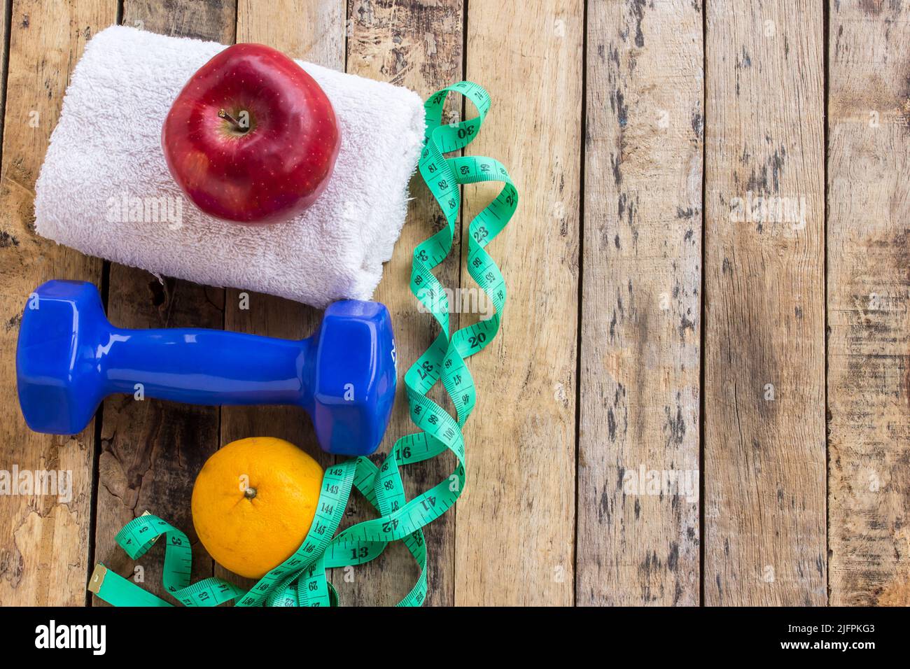 Blaue Hantel, weißes Handtuch, Maßband und roter Apfel auf Holztisch. Fitnesskonzept Stockfoto