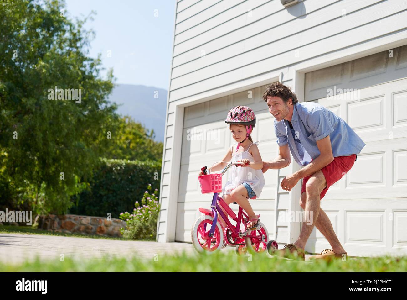 Ich glaube an eure Fähigkeiten. Aufnahme eines jungen Vaters, der seiner Tochter das Fahrradfahren beibringt. Stockfoto