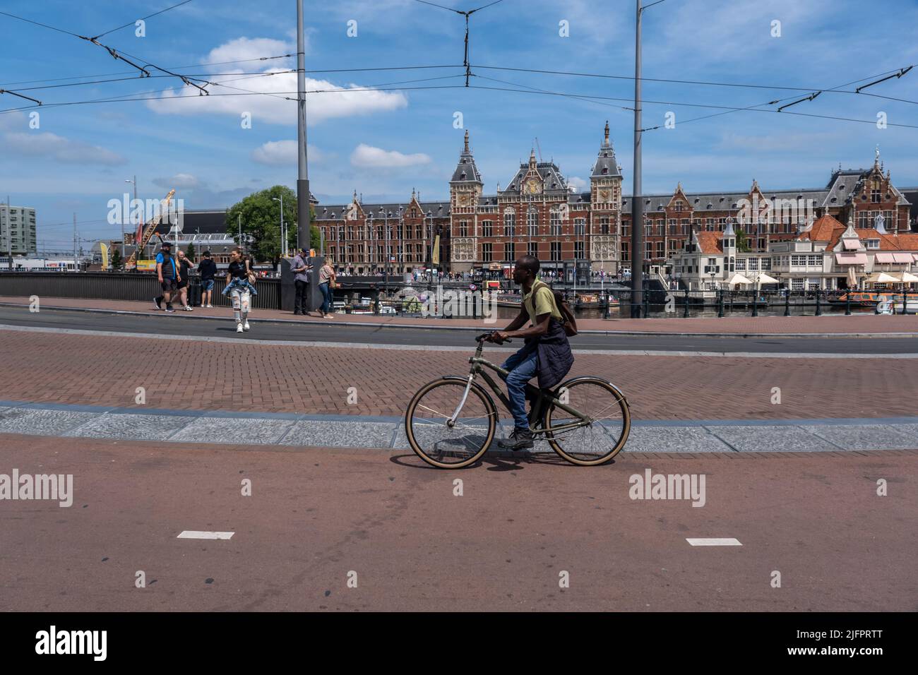 Amsterdam, Niederlande - 21. Juni 2022: Mann fährt Fahrrad mit dem Hauptbahnhof von Amsterdam im Hintergrund Stockfoto