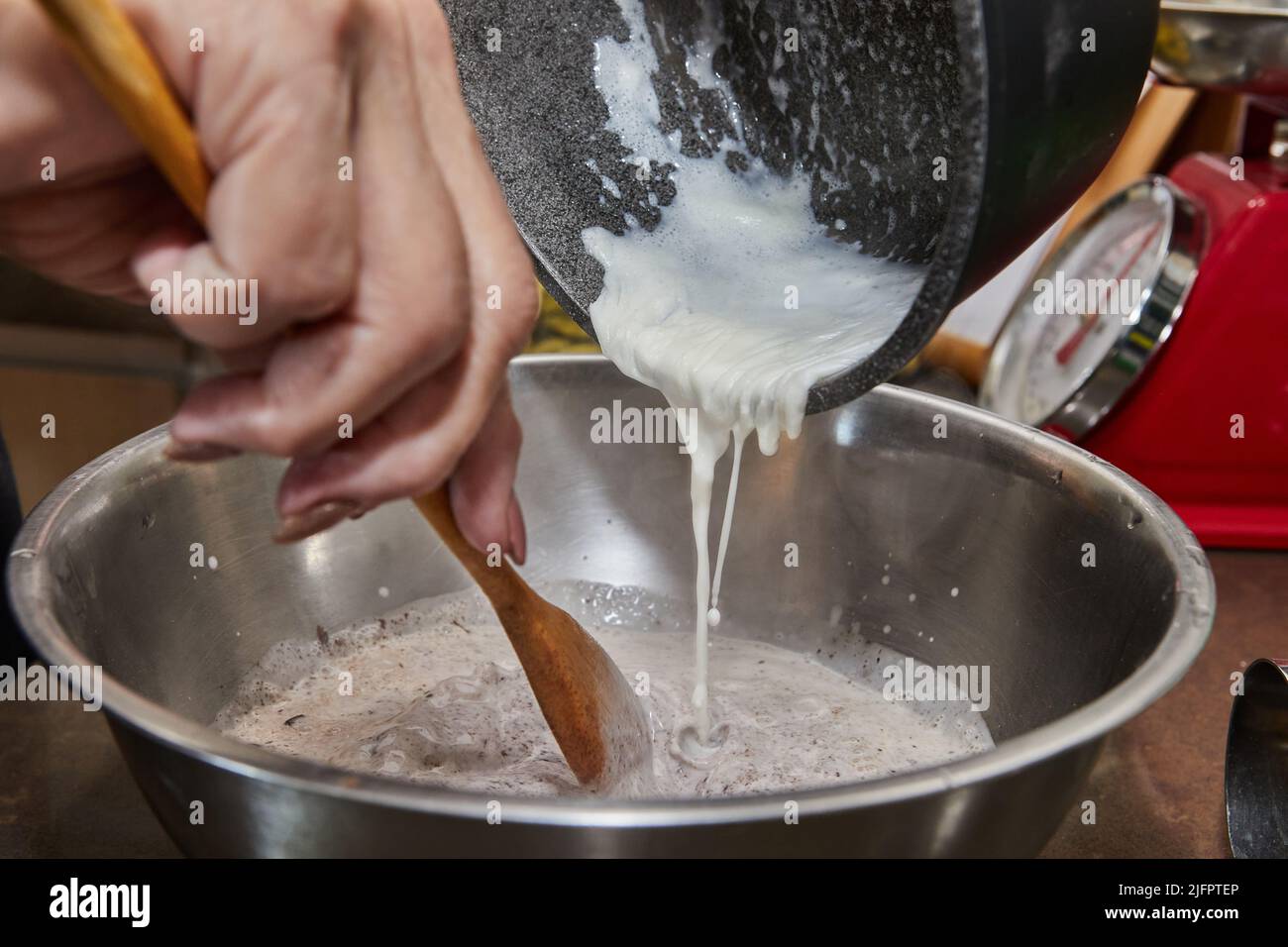 Der Koch gießt Schlagsahne in eine Schokoladenkuchenmischung mit Birnen und Nüssen. Schritt für Schritt Rezept Stockfoto