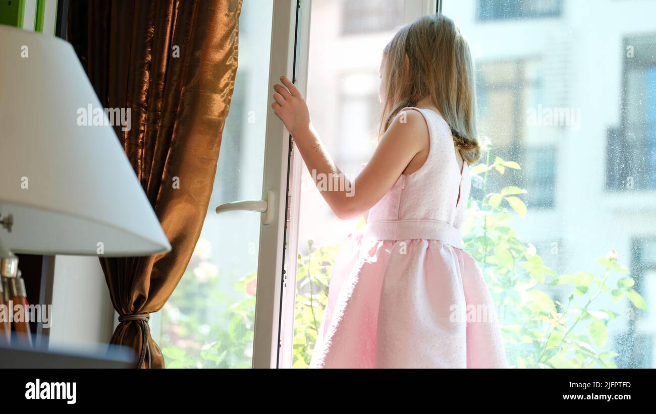 Kleines Kind, das auf der Fensterbank am offenen Fenster steht Stockfoto