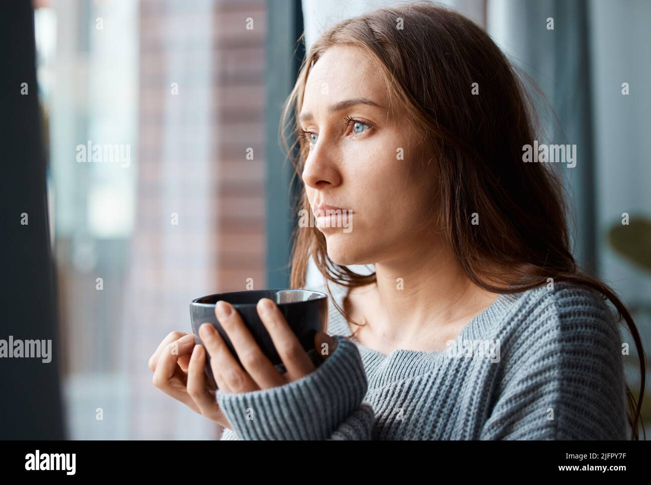 Eine heiße Tasse Tee, um die Seele zu beruhigen. Aufnahme einer unglücklichen jungen Frau, die Tee trinkt, während sie aus dem Fenster schaut. Stockfoto
