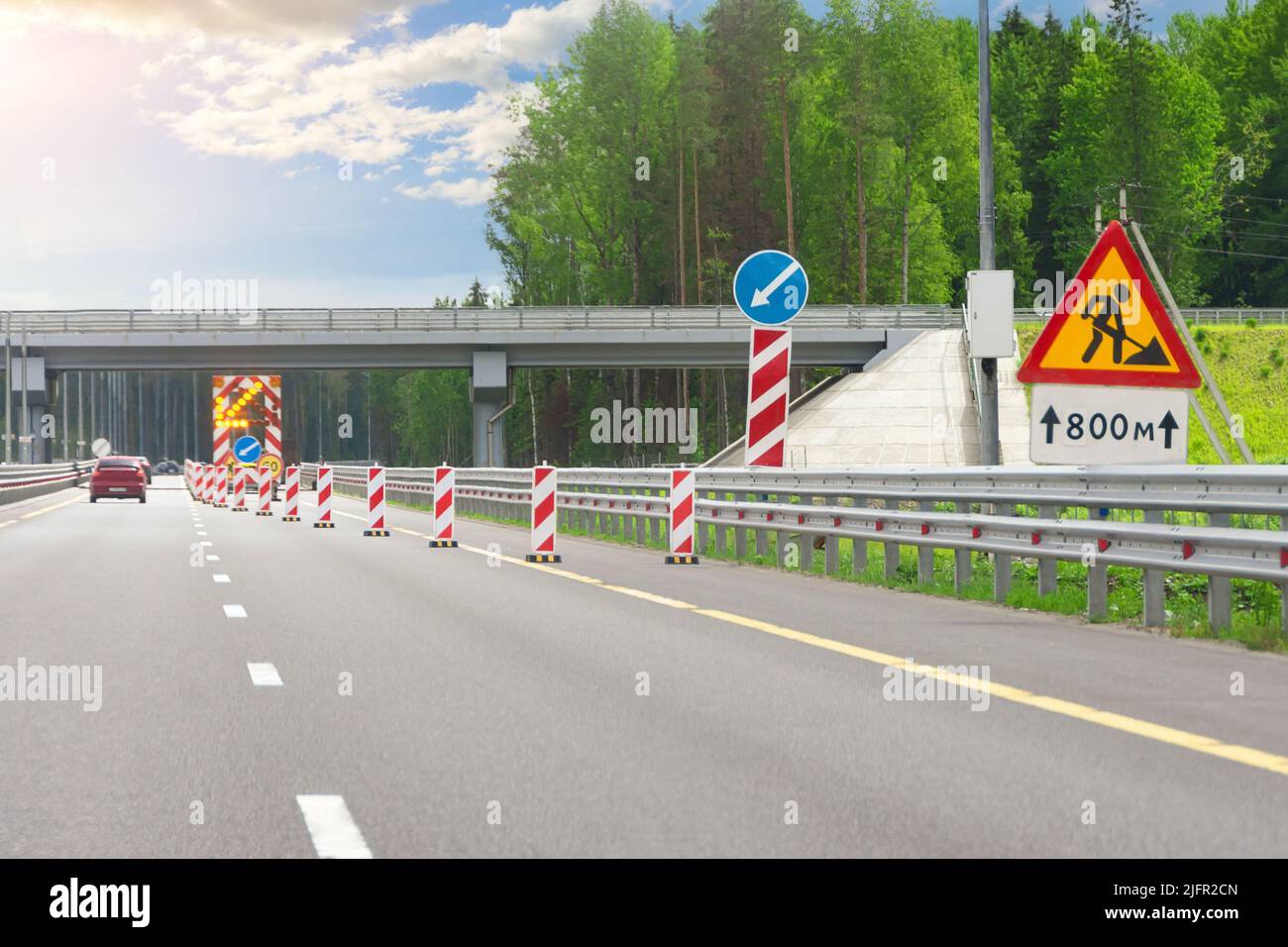 Baustelle, großes helles Mobilschild mit Streifen, Umgehungsrichtung und blinkender gelber Pfeil auf LKW-Anhänger in rechter Fahrspur auf Autobahn Stockfoto