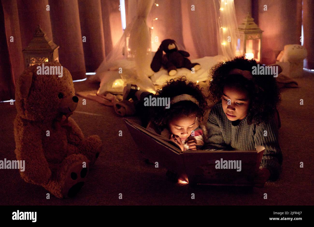 Öffne deinen Geist, öffne ein Buch. Aufnahme von zwei entzückenden kleinen Mädchen, die nachts in einem Zimmer zusammen ein Buch lesen. Stockfoto