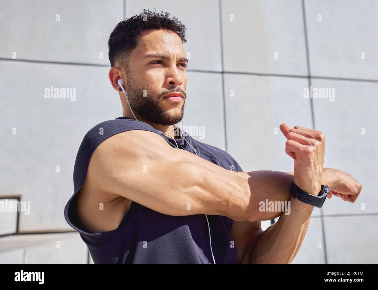 Konzentrieren Sie sich, bevor Sie in Aktion treten. Aufnahme eines sportlichen jungen Mannes, der Musik hört und beim Training im Freien die Arme streckt. Stockfoto