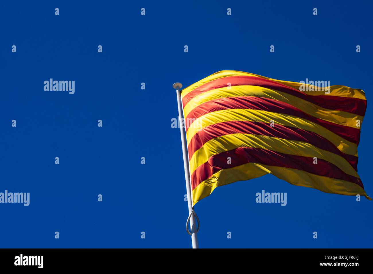 Die Flagge Kataloniens (Spanien) flattert im Wind. Auf der linken Seite des Bildes befindet sich ein großer Bereich mit negativem Raum, der durch den blauen Himmel entsteht. Stockfoto