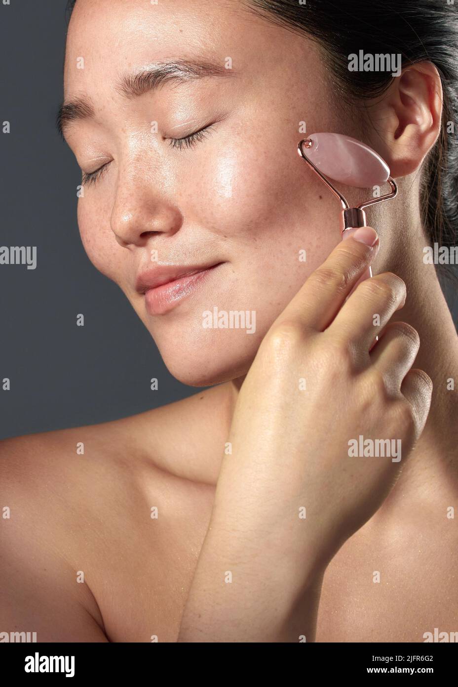 Ich bemerkte, dass meine Haut einen engeren Look hatte und noch jünger aussah. Studioaufnahme einer schönen jungen Frau mit einem Gesichtsroller auf ihrer Haut. Stockfoto