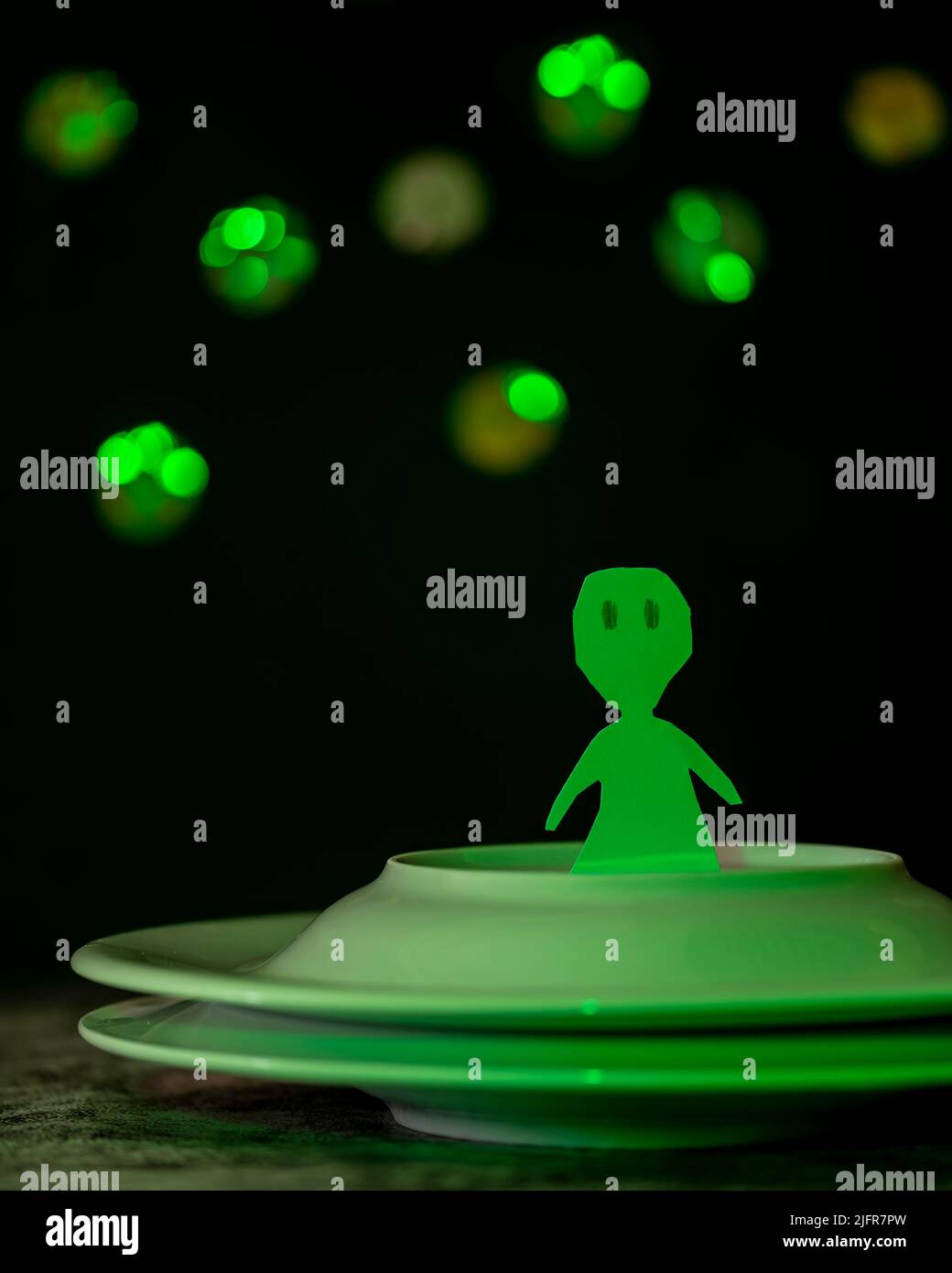 Ein lustiges grünes Alien aus Pappe ist auf einem Raumschiff mit zwei überlappenden Platten Stockfoto
