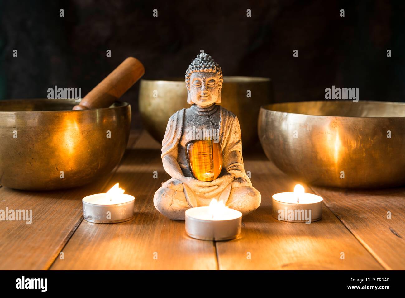 Stillleben mit Klangschalen, Mineralien, Kerzen und einer Buddha-Figur auf Holzbrettern und einem dunklen Hintergrund. Kleiner Altar mit kleiner Kerze beleuchtet Stockfoto