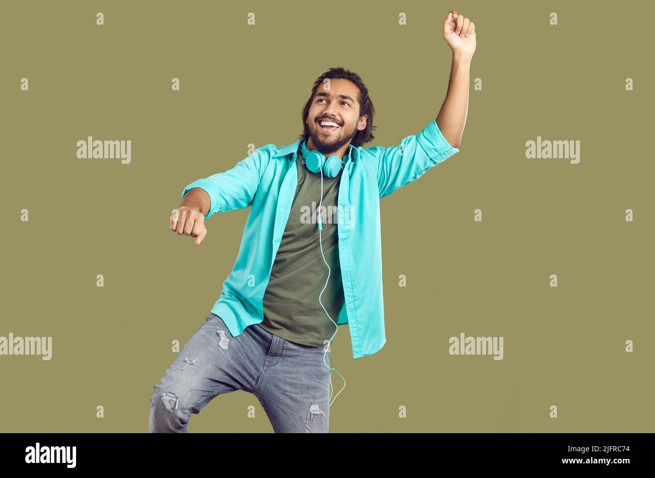 Fröhlicher, lustiger indischer Mann mit Kopfhörern um den Hals tanzt und Spaß auf khaki-Hintergrund hat. Stockfoto