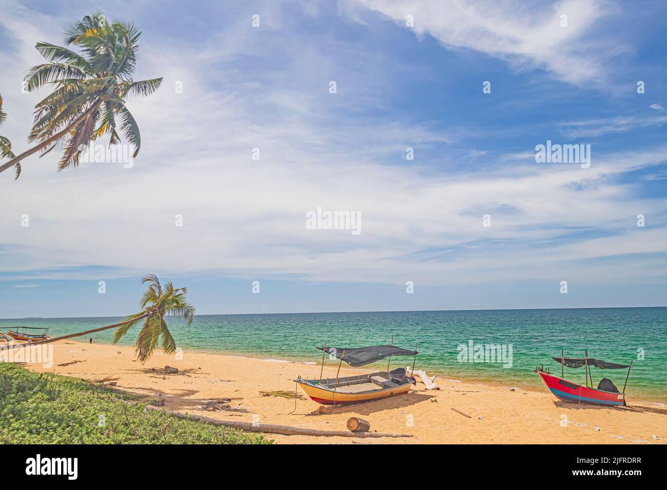 Der Blick auf den Pantai Jambu Bongkok Beach in Terengganu, Malaysia, liegt unter dem wolkenbewachsenen Himmel mit Kokospalmen und Booten am Sandstrand. Stockfoto