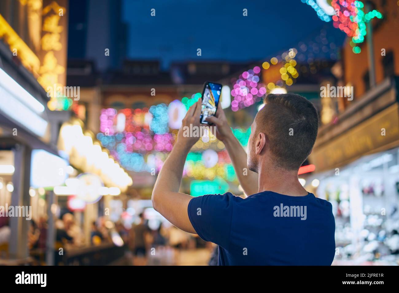 Rückansicht des Mannes beim Fotografieren mit dem Mobiltelefon auf einer farbenfrohen Straße. Tourist in Chinetown in Singapur. Stockfoto