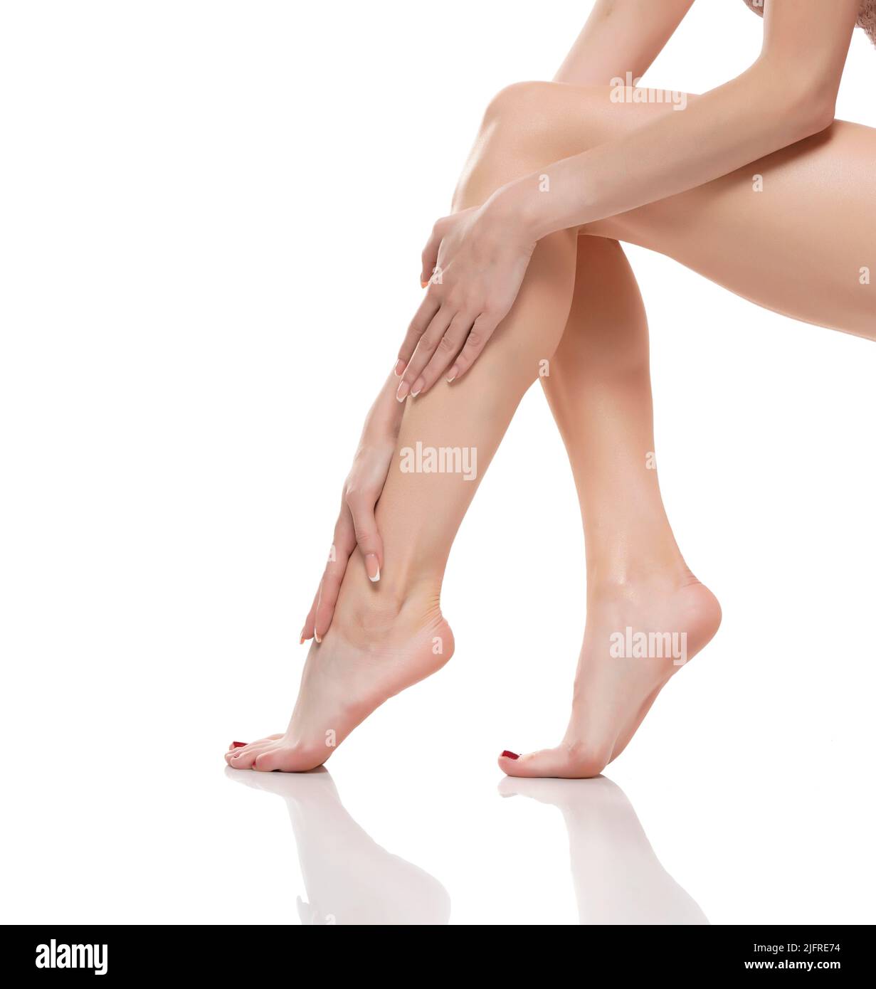 Die junge Frau berührte ihre glatten langen Beine und setzte nach dem Rasieren ihrer Beine eine Feuchtigkeitscreme auf. Stockfoto