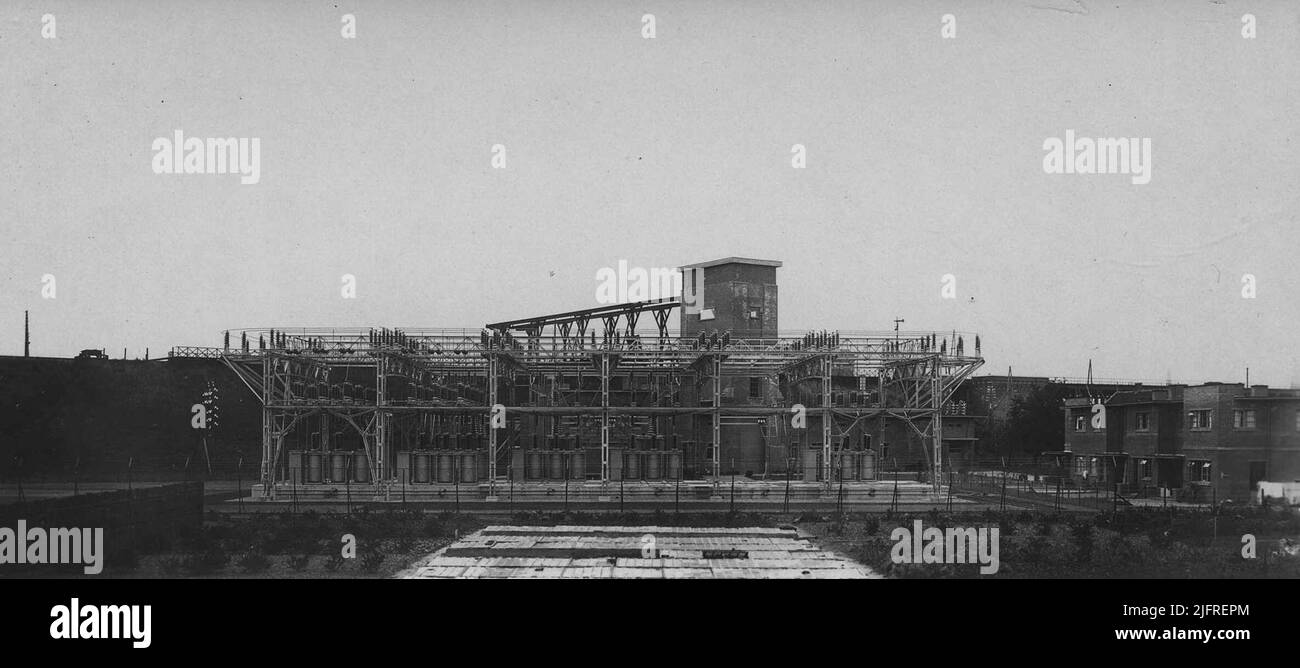 Bestimmung der Transformatoren von Willem Smit & Co's Transformatorenfabriek NV im 'Provisorium' der 50 kV (50 Kilovolt - 50.000 Volt) Substitution/Distribution Station der Provincial Geldersche Electriciteit Maatschappij (PGEM). Im Hintergrund die Spoorbaan Nijmegen-Arnhem mit der Transportverbindung vom Bahnhof Lent zum Hebeturm des Kontrollgebäudes. Direkt die angrenzenden Dienstleistungshäuser Stockfoto