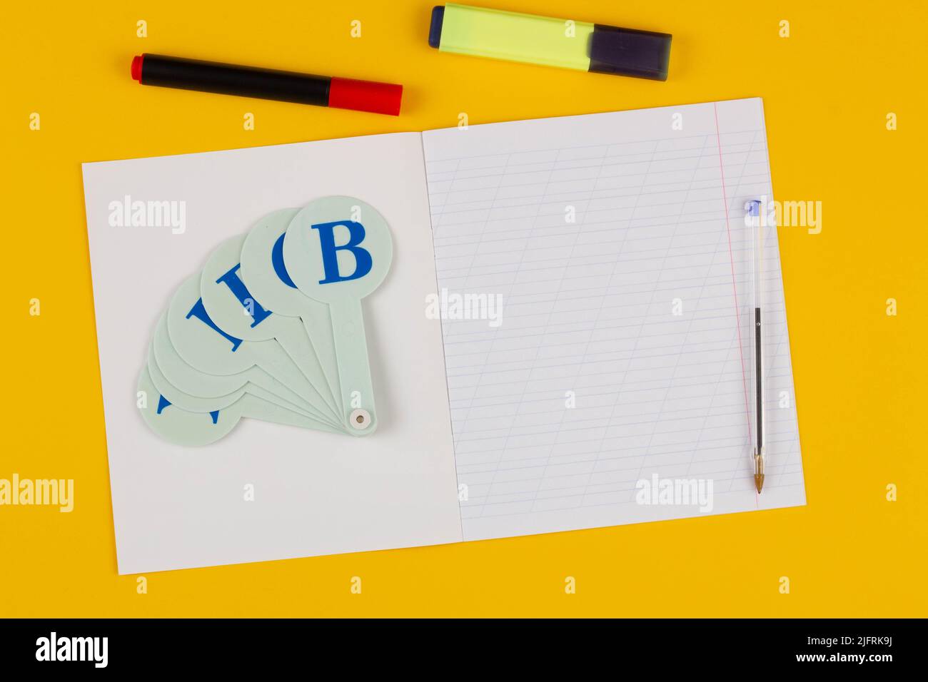 Schulnotizbuch auf gelbem Hintergrund mit Platz für Text, bunten Markern, englischem Alphabet. Zurück zur Schule. Leeres Blatt Papier mit schräg Stockfoto